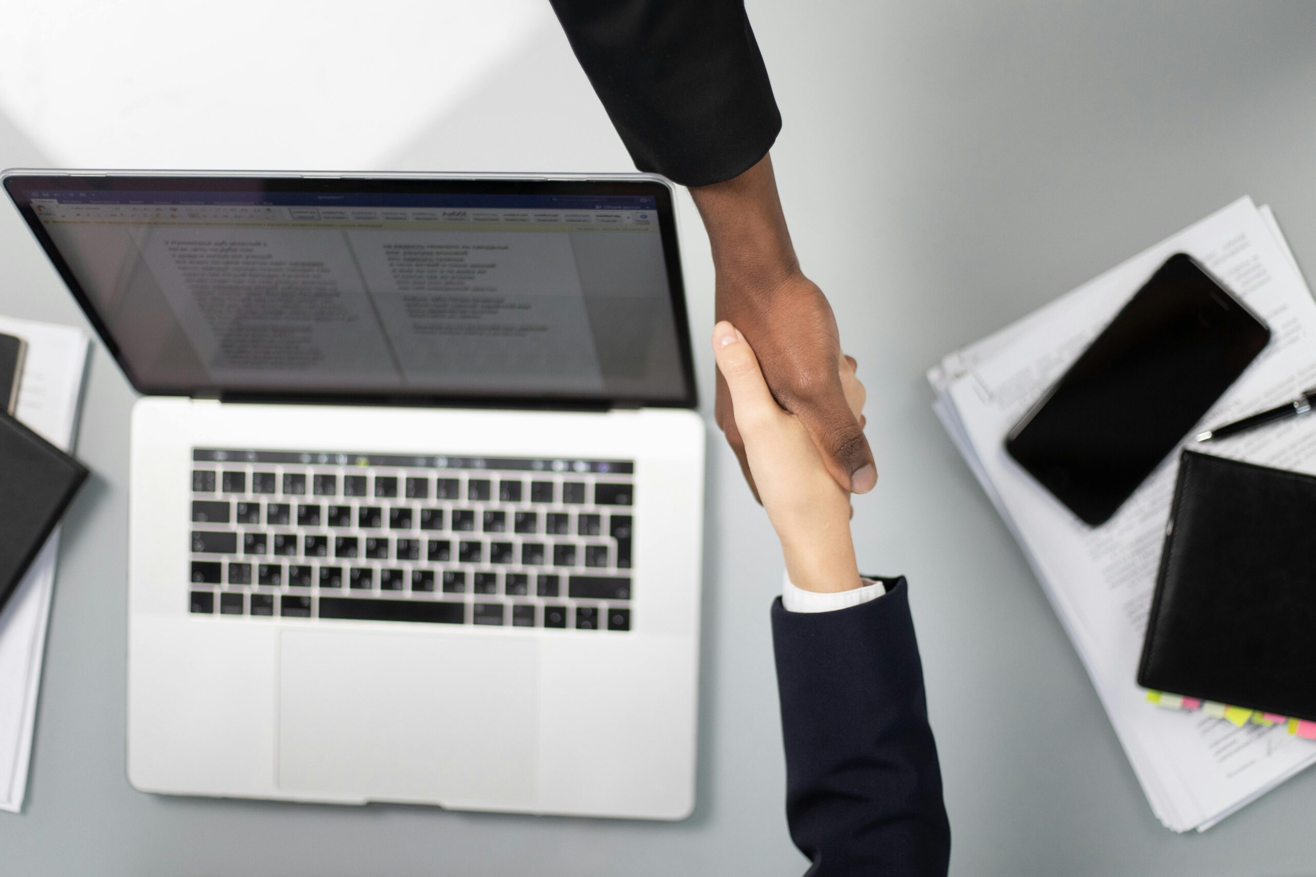 Blog Overhead view of a professional handshake over a laptop, symbolizing business agreement.